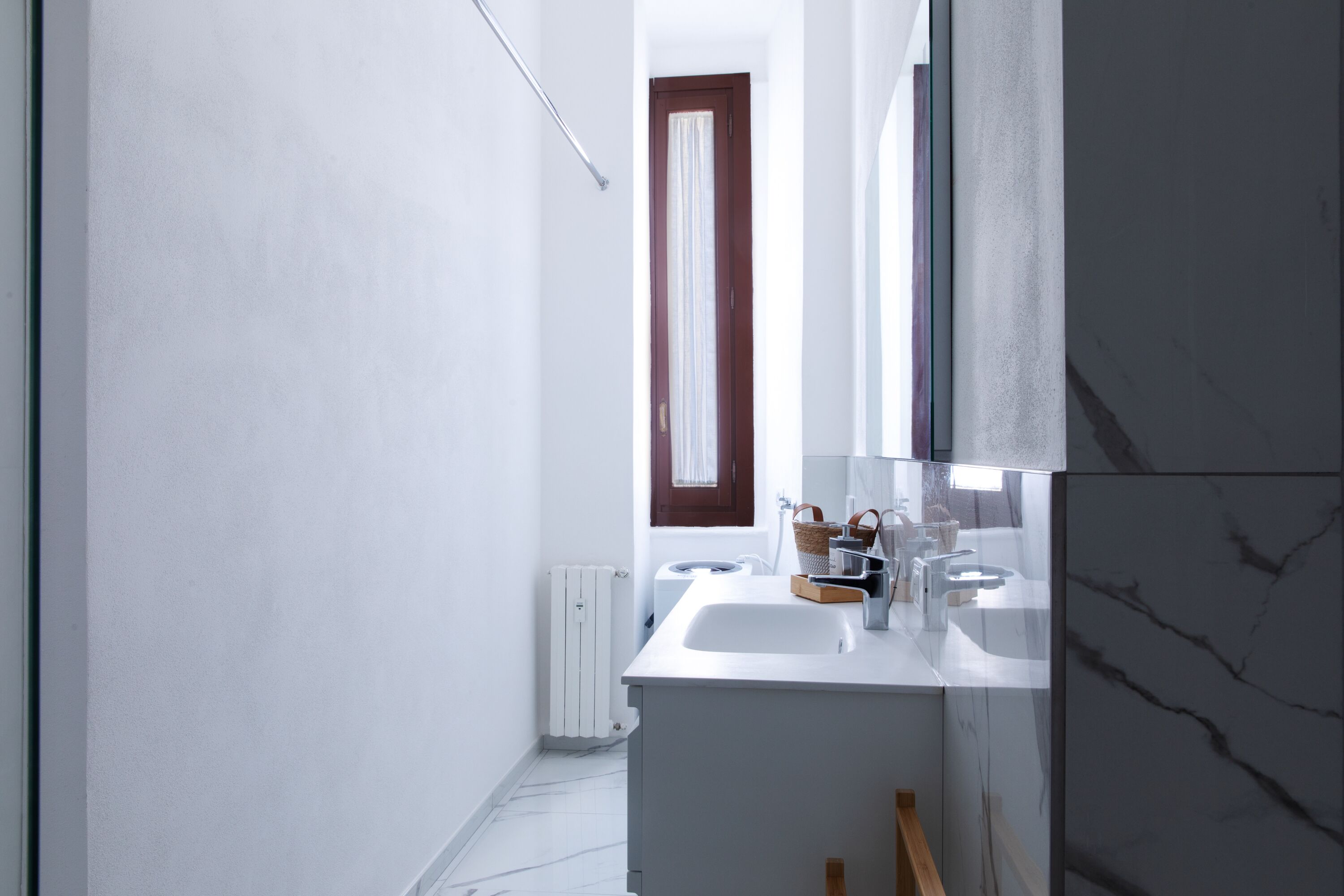 Un bagno moderno con lavandino bianco, specchio e pannello marmorizzato.