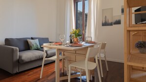 En moderne stue med en grå sofa, et træspisebord med hvide stole, og et vindue med gardiner.