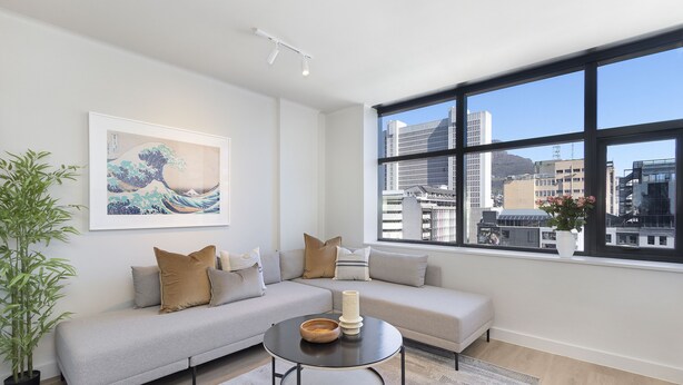 Ein modernes Wohnzimmer mit einem grauen Sofa, einem runden Couchtisch und einem großen Fenster mit Blick auf die Stadt.