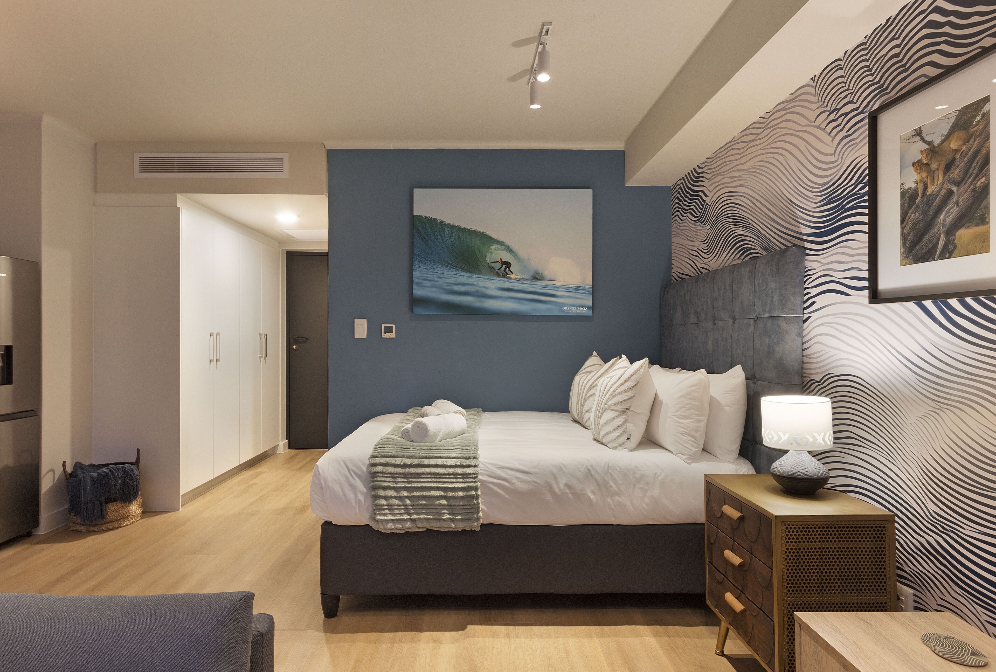 Ein modernes Schlafzimmer mit einem großen Bett, einem Nachttisch mit Lampe, einem gerahmten Bild an der Wand und einer Wand mit ZEBRA-Muster.