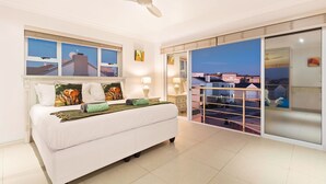Un dormitorio con cama, ventilador de techo y vistas a la ciudad a través de amplios ventanales.