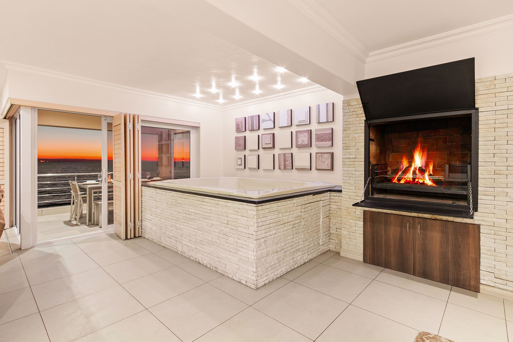 A modern living room with a fireplace, a large window with a view of the sunset, and a bar area with a glass top.