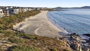 Vista costera con playa de arena, un paseo de madera y edificios a lo largo de la orilla.