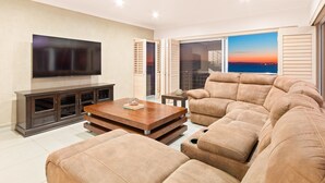 Una sala de estar moderna con un televisor de pantalla plana, una mesa de centro de madera y un sofá seccional beige grande.
