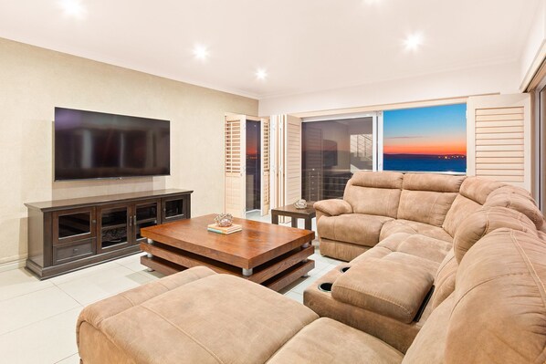 A modern living room with a flat-screen TV, a wooden coffee table, and a large beige sectional sofa.