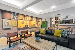 Un salon moderne avec un canapé en cuir noir, une table basse en bois et des œuvres d’art accrochées aux murs.