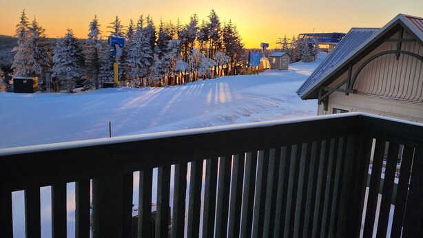 Lumipeitteinen maisema, jossa on puinen terassi ja näkymä auringonlaskuun.
