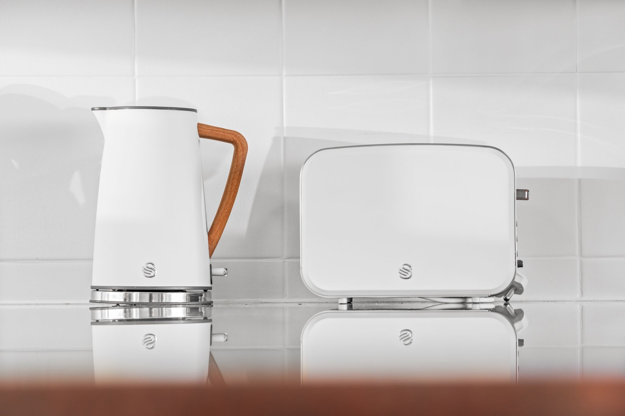 Una cocina con una tetera blanca y un tostador blanco sobre una superficie reflectante.