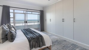 Un dormitorio con una cama grande, un ventilador de techo y vistas al océano a través de un ventanal.