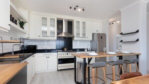 Una cocina moderna con armarios blancos, un refrigerador de acero inoxidable, una mesa de madera y taburetes de bar.