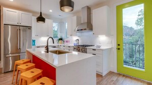 A modern kitchen with white cabinetry, a central island with stools, stainless steel appliances, and a bright green door. - The Ultimate Hip-Hop Haven – Rooftop Patio (Nashville)