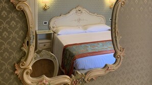 A room with a large ornate mirror, a bed with floral bedding, and a nightstand with a lamp. - Hotel La Residenza (Venice)