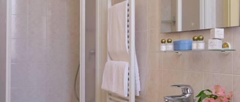 A modern bathroom with a glass shower enclosure, a white sink, and a vanity with a mirror. There are toiletries on the shelf and a towel rack with white towels.