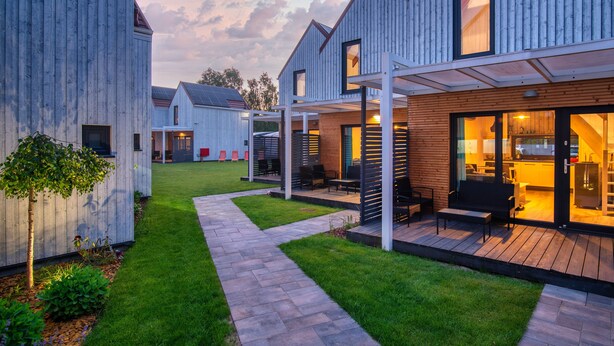 A modern house with a covered patio, a well-maintained lawn, and a visible kitchen area. - Domki Fantazja Dębki (Krokowa)