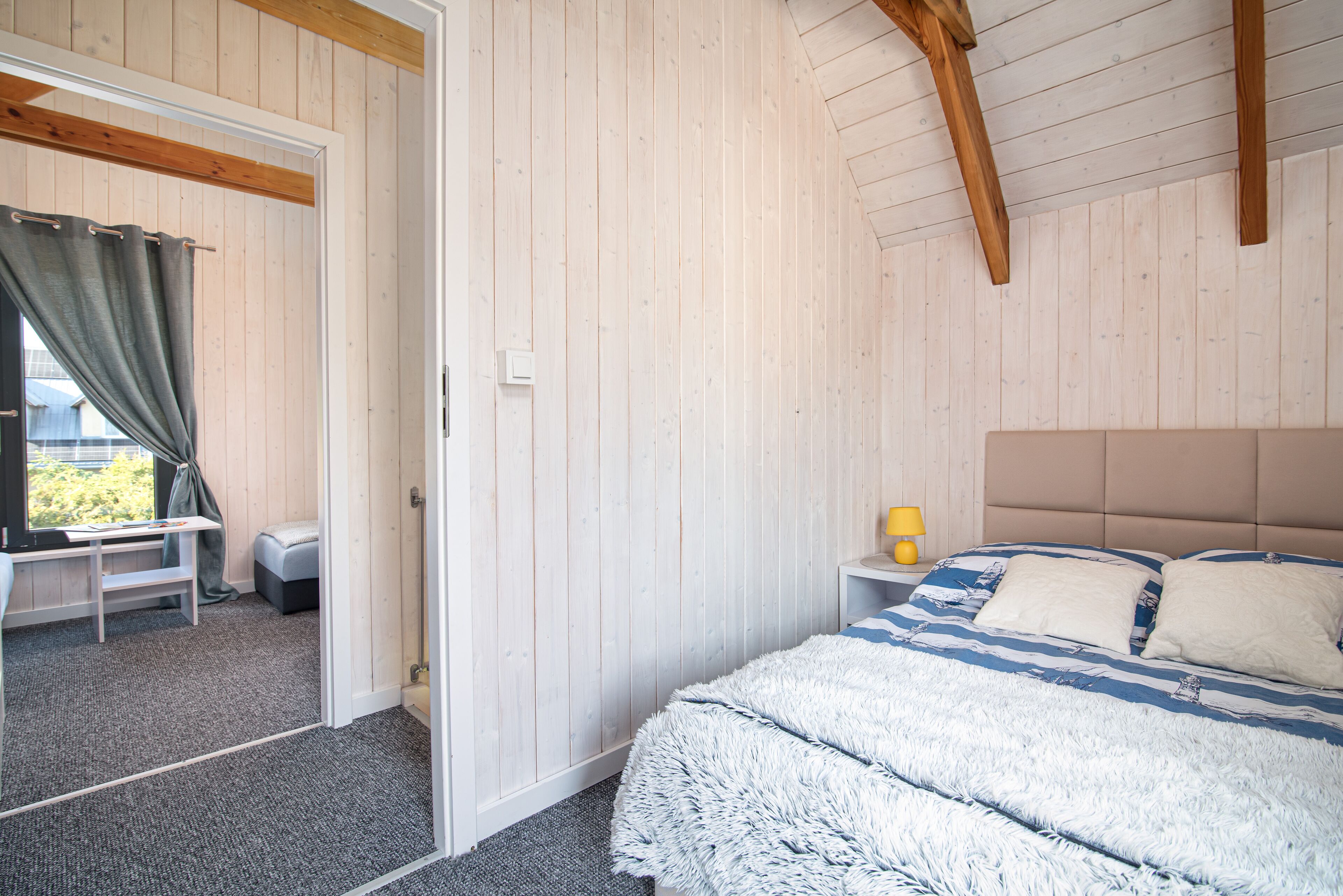Une chambre à coucher comprenant un lit, une table de chevet, une lampe, une fenêtre avec des rideaux et une vue sur l’extérieur.