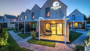 A modern building with a sign reading "Fantazija." It features a covered outdoor seating area with a table and chairs, and a well-maintained lawn. - Domki Fantazja Dębki (Krokowa)