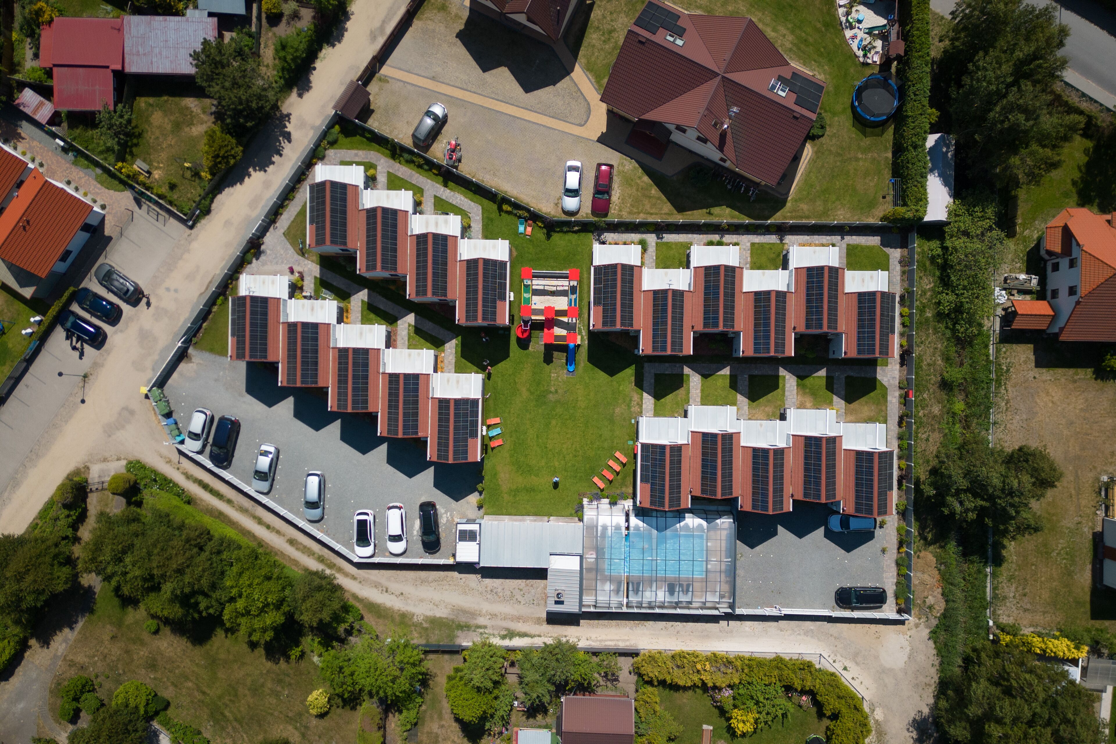 An aerial view of a residential area with multiple houses, a swimming pool, and a parking lot.