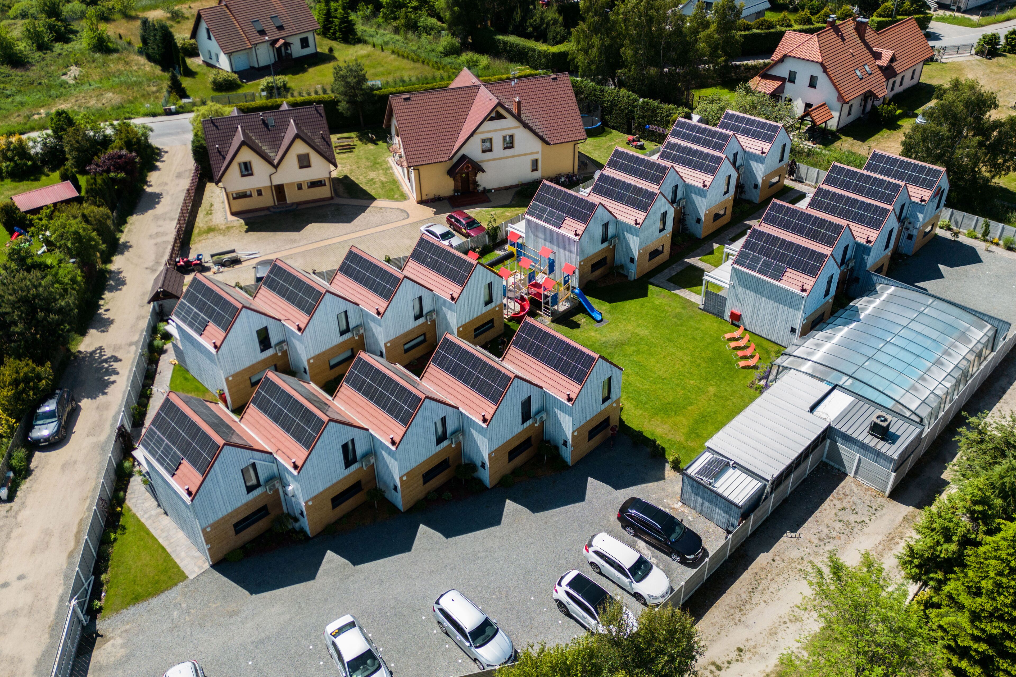 Un barrio residencial con varias casas, algunas con paneles solares, un parque infantil y un invernadero.