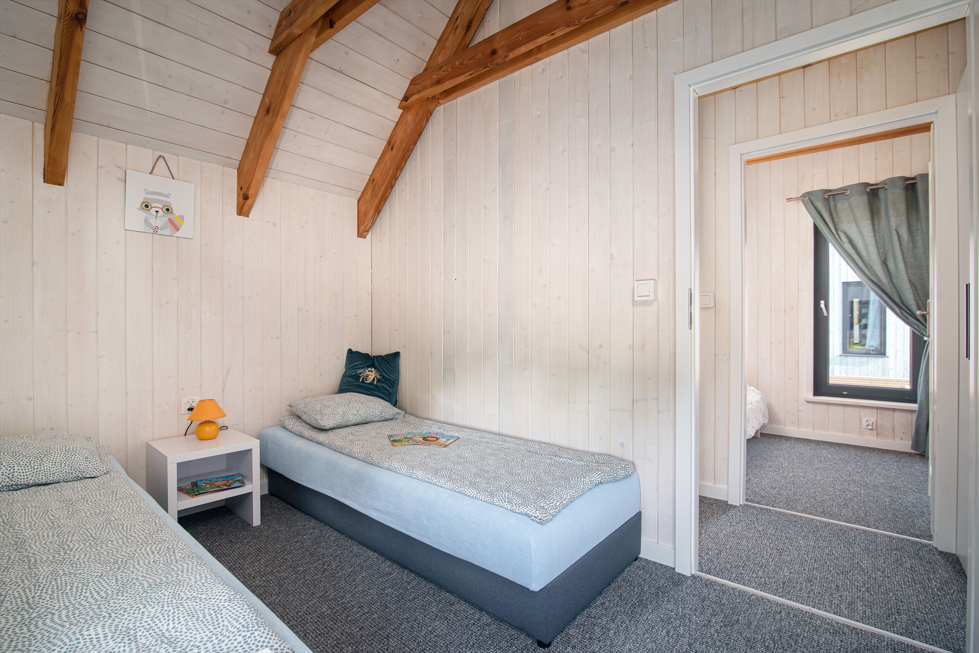 Een slaapkamer met een eenpersoonsbed, nachtkastje, raam met gordijnen en een houten plafond.