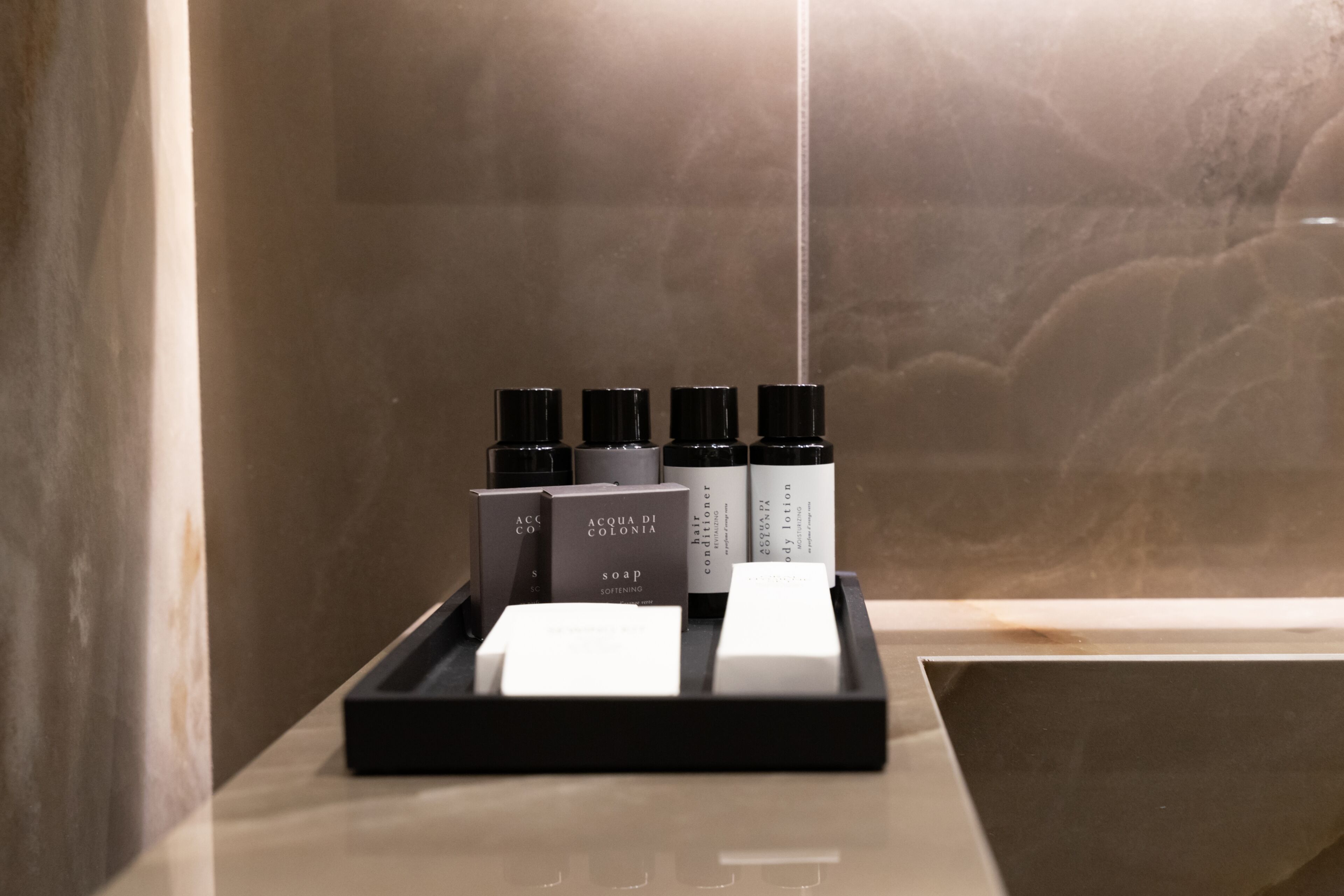 A bathroom with a marble wall, a black tray holding various toiletries, and a white sink.