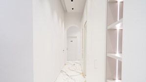 A narrow hallway with white walls and a marble floor leading to a door marked '404'. Shelves are built into the wall on the right. - InSogno Suites (Naples)
