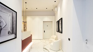 A modern hallway with a marble floor, a reception desk, a white door labeled '401', and a seating area with two chairs. - InSogno Suites (Naples)
