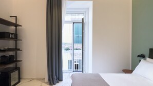 A bedroom with a bed, a shelf unit, a window with curtains, and a view of the outside balcony. - InSogno Suites (Naples)