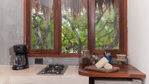 Eine Küche mit Kaffeemaschine, Gasherd, Schneidebrett und einem Fenster mit Blick auf Bäume.