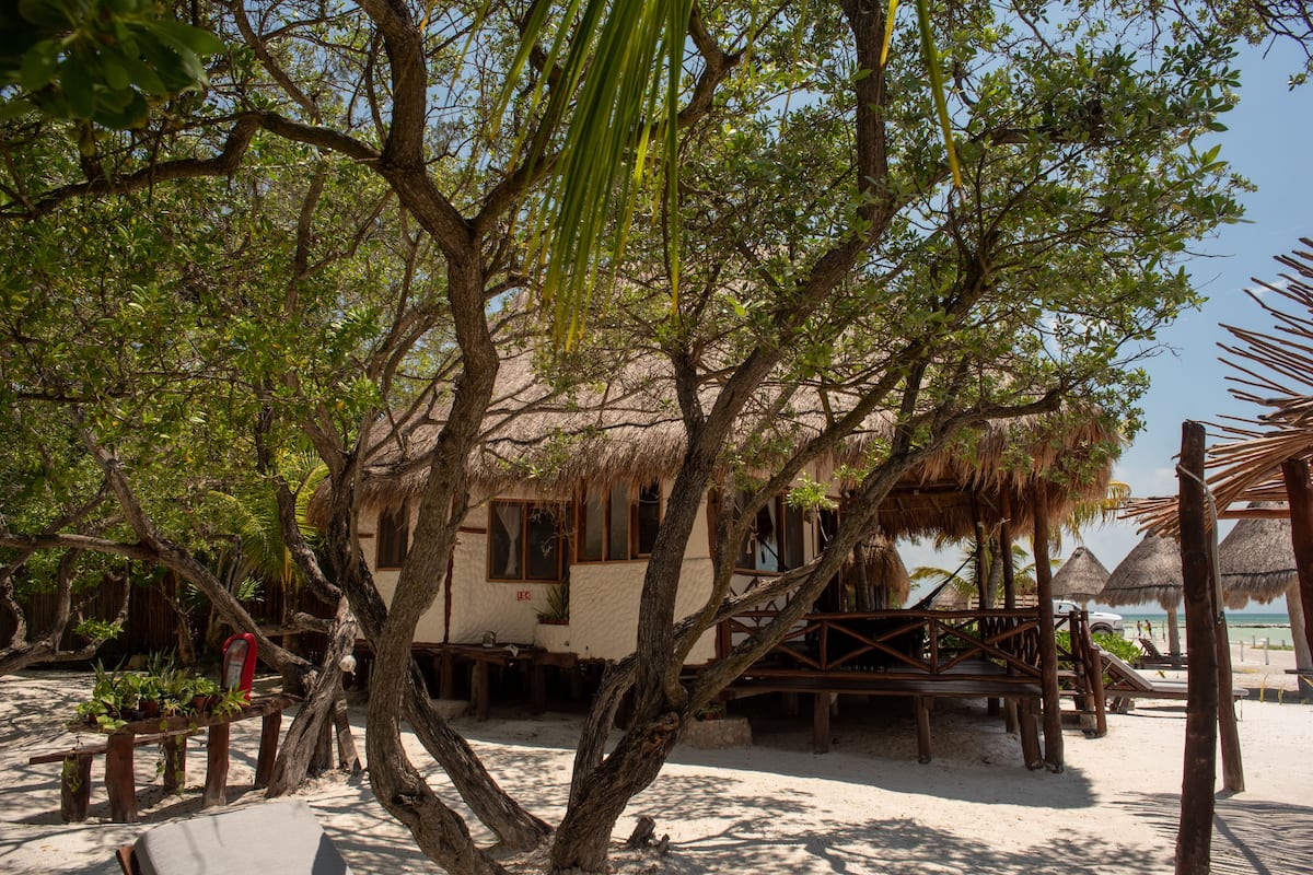 A beach house with a thatched roof, surrounded by trees and a wooden deck.