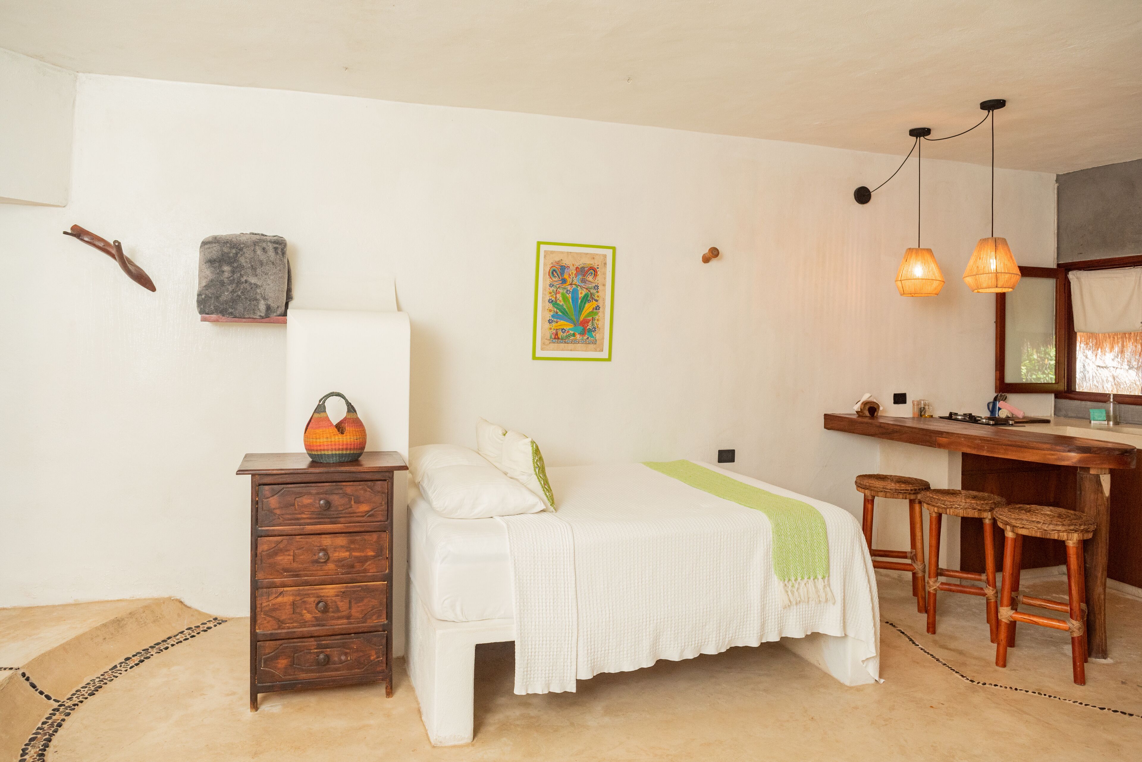 Een slaapkamer met een bed, een houten dressoir en een klein bureau met krukjes.