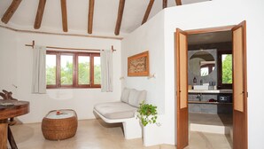 Ein Zimmer mit Holzboden, einem fenster mit Vorhängen, einer Couch, einem kleinen Tisch, einem Spiegel und einer Pflanze.
