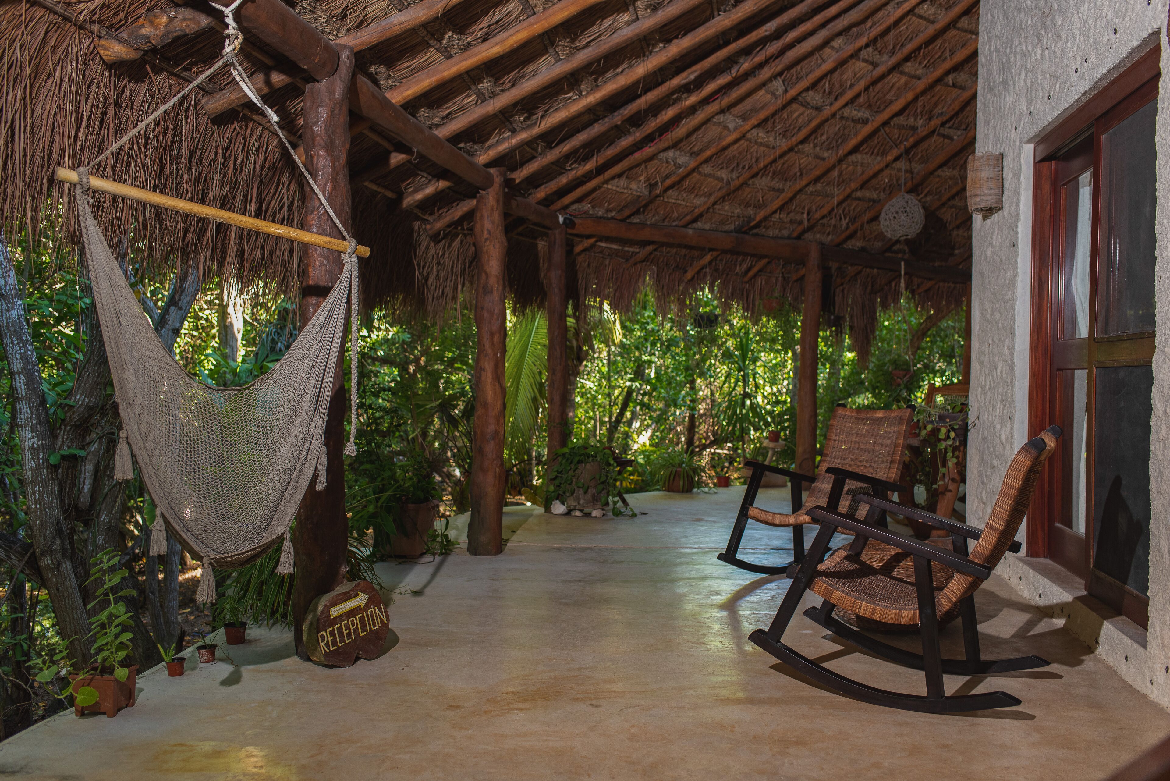 A covered outdoor area with a hammock, rocking chairs, and potted plants.