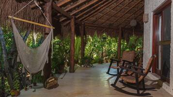 A covered outdoor area with a hammock, rocking chairs, and potted plants.