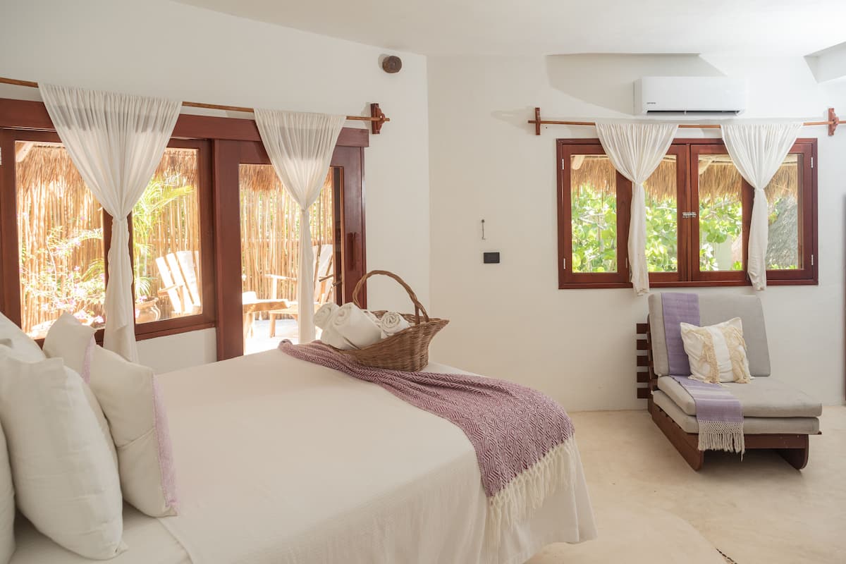 A bedroom with a bed, a chair, a window with curtains, and a wall-mounted air conditioner.