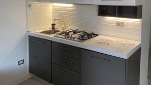 Une cuisine de taille réduite avec des meubles blancs, une cuisinière à gaz et un pare-feu en carreaux.