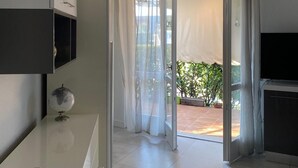 Une pièce moderne et bien éclairée, dotée d’une porte-fenêtre coulissante donnant sur un espace extérieur, d’une petite table sur laquelle se trouve un globe terrestre et d’un téléviseur placé à droite.
