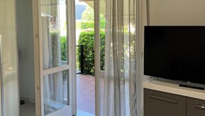 Un salon moderne équipé d’un téléviseur, d’une porte-fenêtre coulissante donnant sur un balcon et d’un appareil de climatisation fixé au plafond.