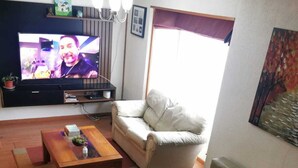Olohuone, jossa on taulutelevisio, sohva, sohvapöytä ja ikkuna, jossa on verho.