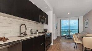 Une cuisine moderne avec des meubles de couleur sombre, un plan de travail blanc et une vue sur la ville grâce à de grandes fenêtres.