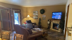 A cozy living room with a leather sofa, a coffee table, a fireplace, and a television. - Quiet apt-cabin on Deschutes River (Bend)