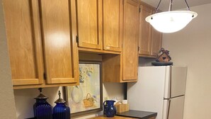 A kitchen with wooden cabinets, a black countertop, a white refrigerator, and a tiled floor. - Quiet apt-cabin on Deschutes River (Bend)