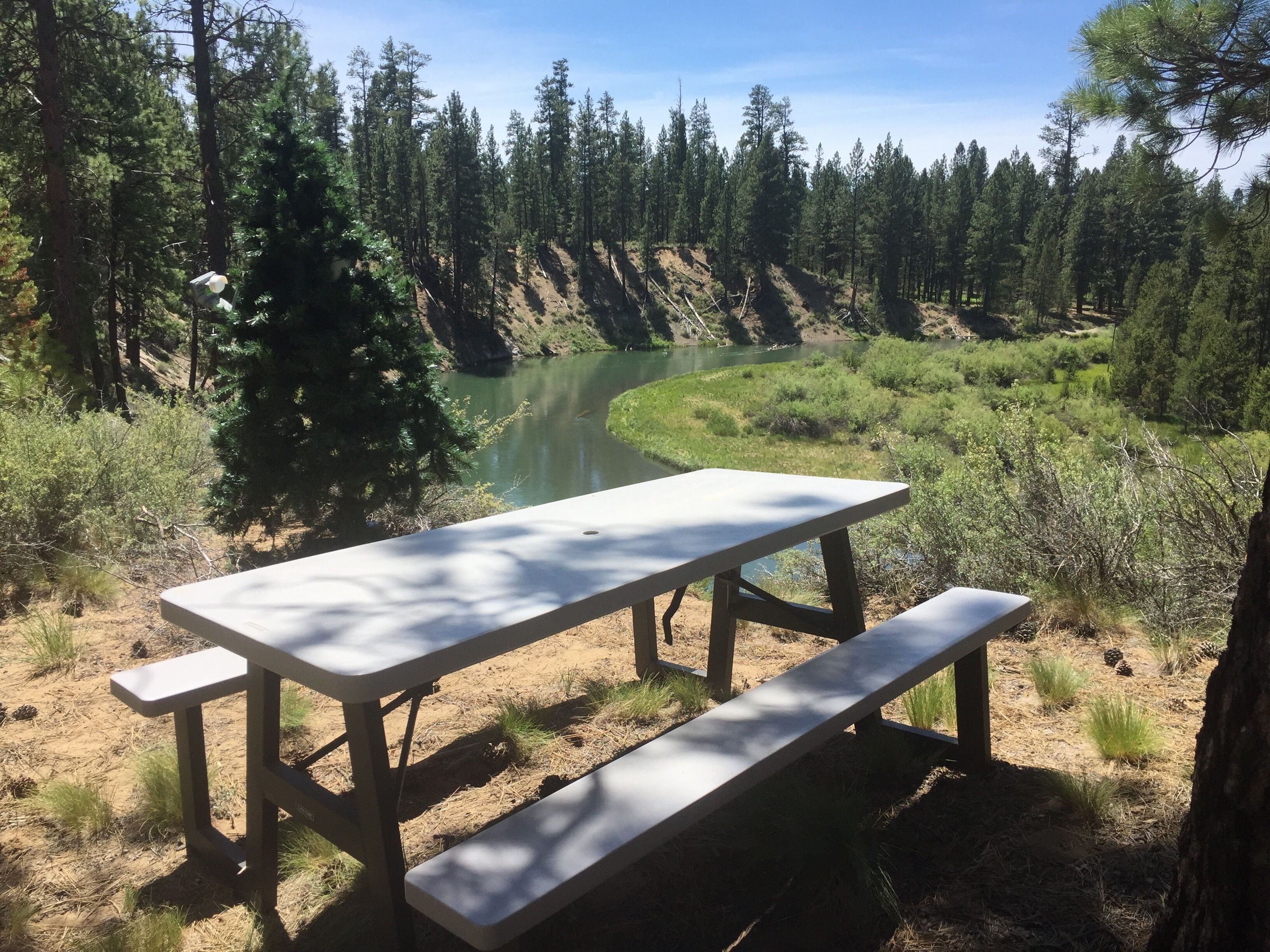A picnic table with benches in a forested area with a river in the background.