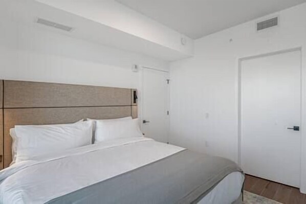 Une chambre à coucher avec un lit, une tête de lit en bois, une porte blanche et un interrupteur sur le mur.