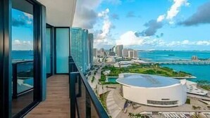 A modern hotel room with a balcony overlooking a coastal cityscape and a marina.