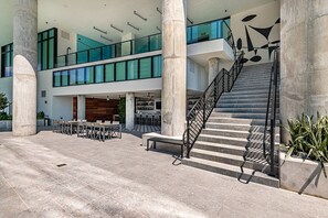 A modern building with a central staircase, large columns, and a dining area with tables and chairs. - Spacious & Stylish Studio in Dowtonw #1406 (Miami)