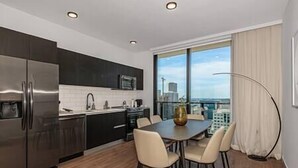 A modern kitchen with dark cabinetry, a stainless steel refrigerator, and a dining area with a table and chairs.