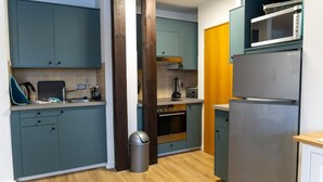 Une cuisine de taille réduite avec des meubles de couleur turquoise, un réfrigérateur en acier inoxydable et un four à micro-ondes placé sur le dessus.