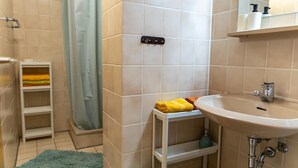 Une salle de bain avec une douche, un lavabo, un miroir et une étagère avec des serviettes.