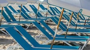 Rows of blue lounge chairs with white canopies on a sandy beach.