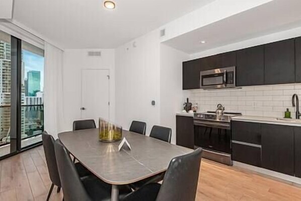 A modern kitchen with dark cabinets, a stainless steel microwave, and a large dining table with chairs.